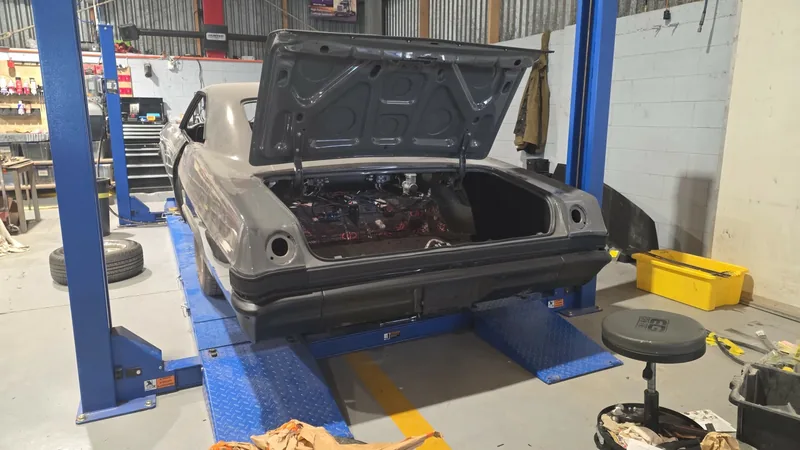 The finished grey 1965 Impala with the boot open, up on the two-post hoist at Kohl Customs