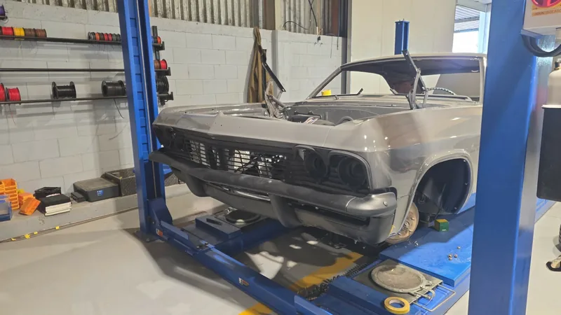 Front of the finished grey 1965 Impala with the grille, bumper and trim blacked out, up on the hoist at Kohl Customs