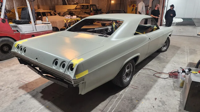 Rear three-quarter of the 1965 Impala in primer with the tail light openings taped off