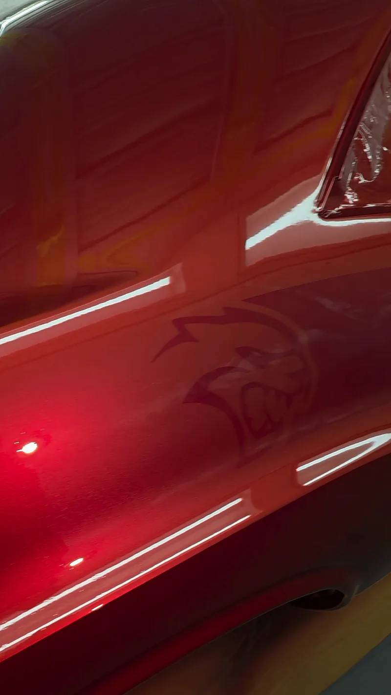 The custom metallic red and the ghosted Hellcat logo on the 1971 Dodge Challenger, seen as the light moves across the panel