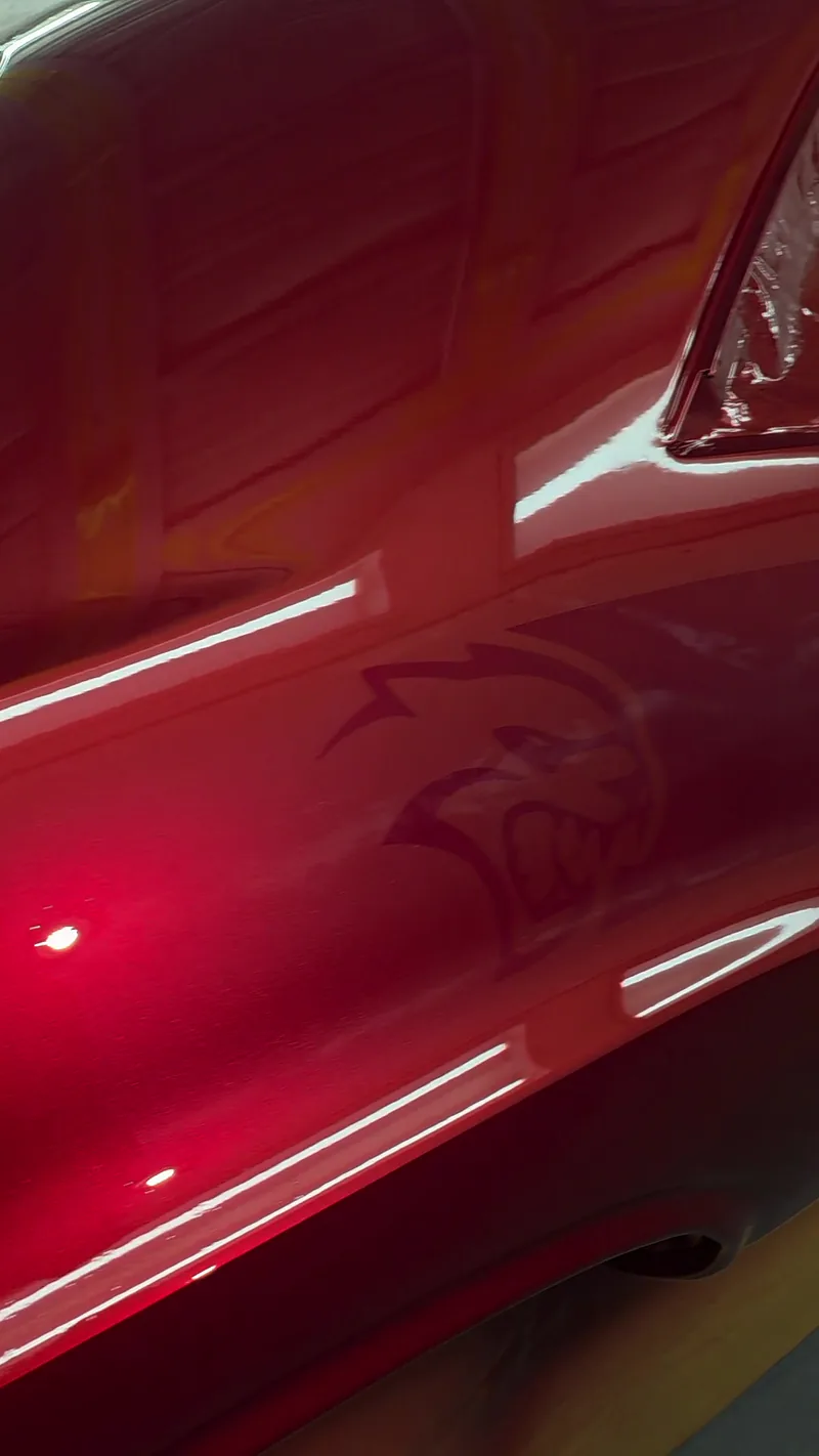 The Hellcat logo ghosted into the metallic red paint on the quarter panel of the 1971 Dodge Challenger