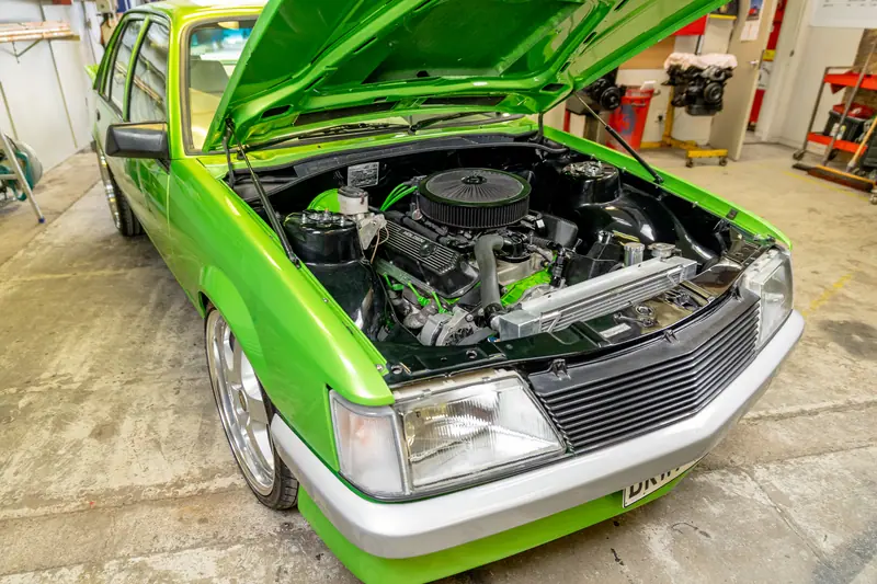 Three-quarter view into the engine bay of the restored VH Commodore with the bonnet up in the workshop