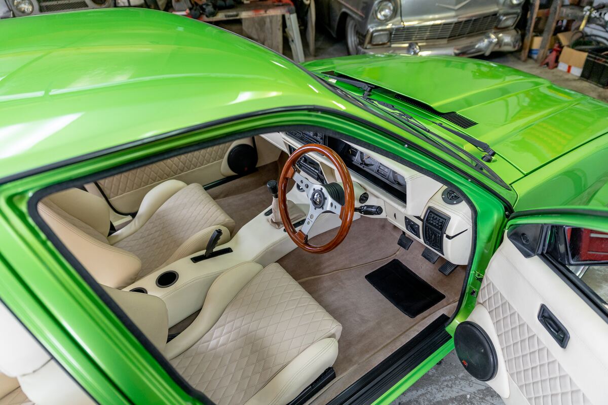 Looking down into the retrimmed cabin of the VH Commodore — cream diamond-stitch seats, wood-rim steering wheel and original dash