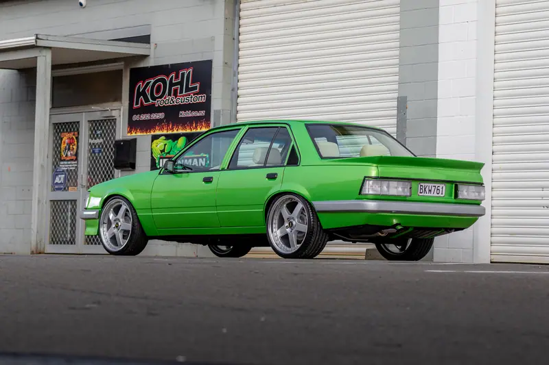 Rear three-quarter view of the green VH Commodore parked outside the Kohl Customs workshop signage