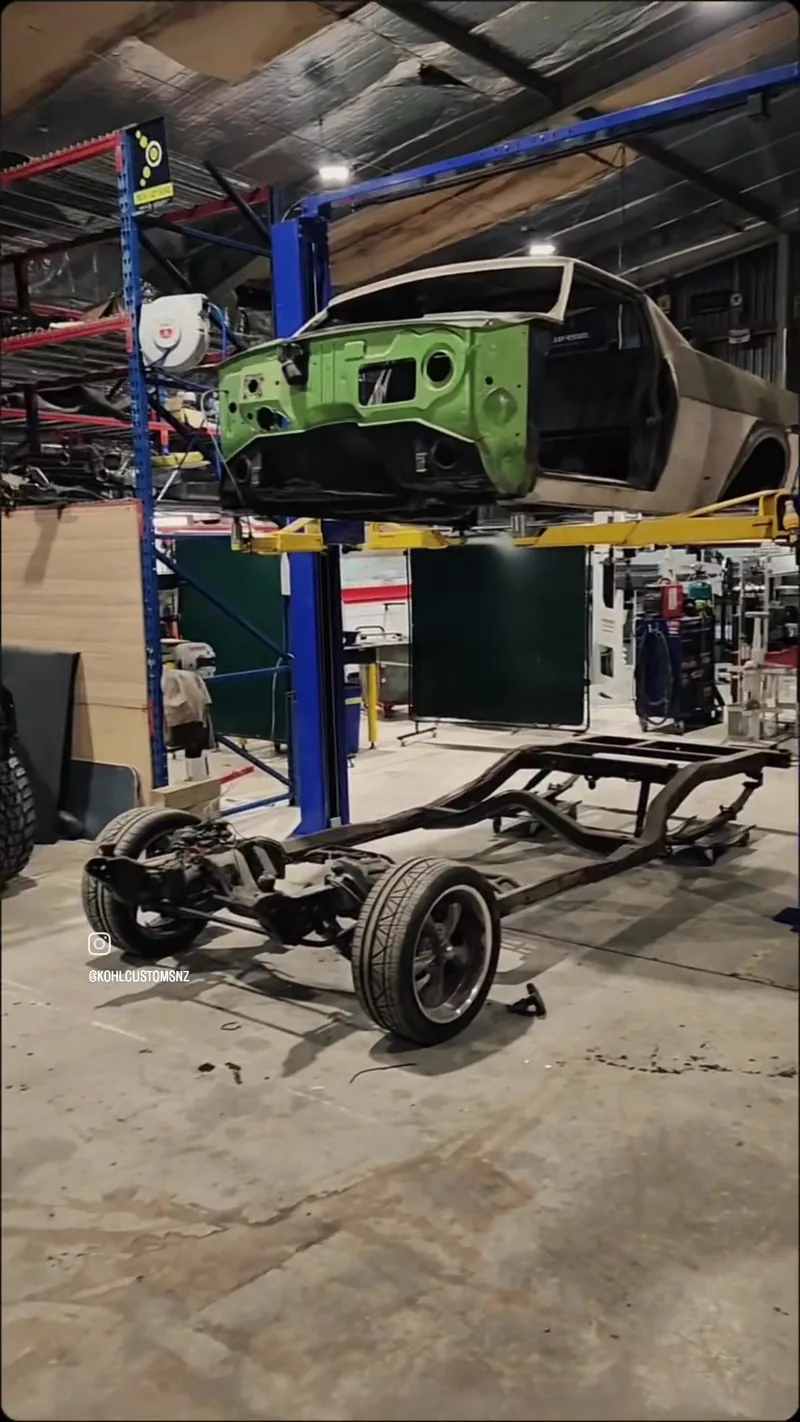 The fabricated chassis for the HJ Holden ute on the workshop floor with the body raised on the hoist above